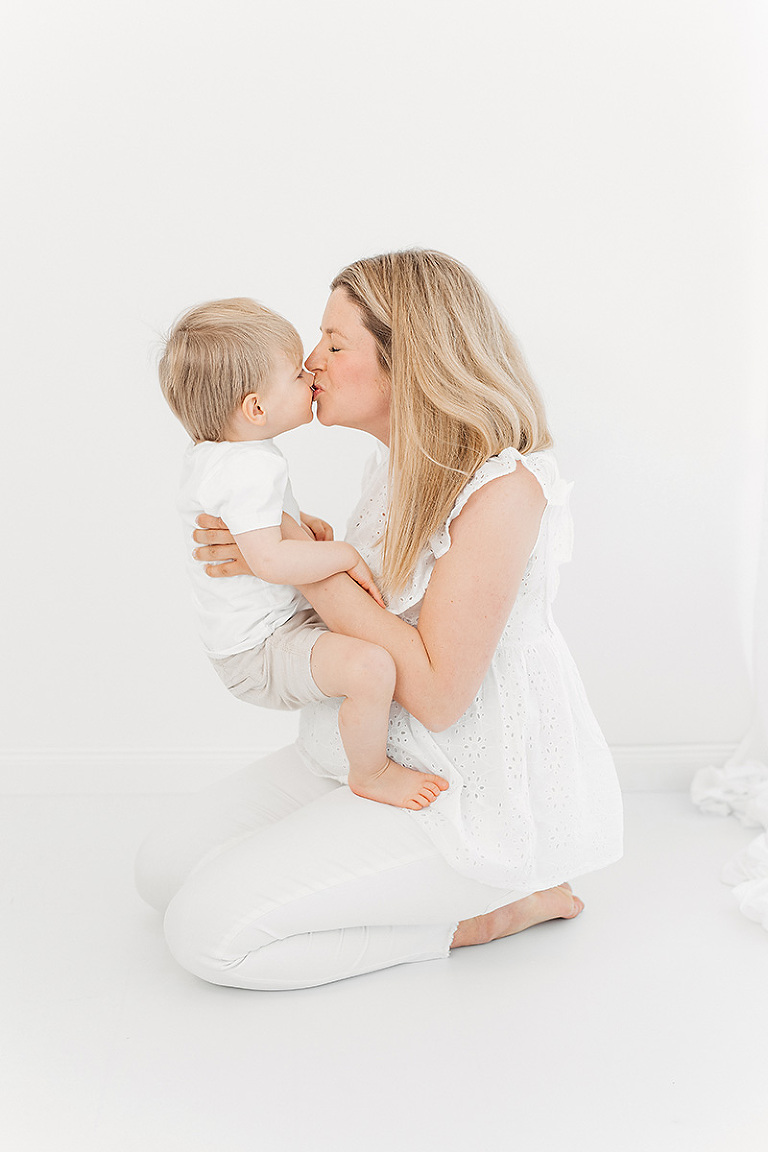 Babybauchshooting Bielefeld: Schwangere Mama kniet auf dem Boden und gibt ihrem Sohn einen Kuss auf den Mund