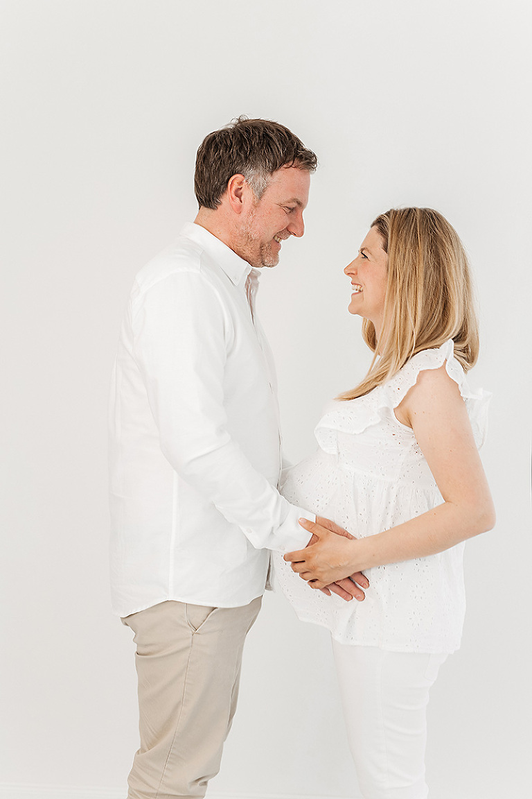 Babybauchshooting Bielefeld: schwangere Frau steht ihrem Mann gegenüber und beide lächeln sich an