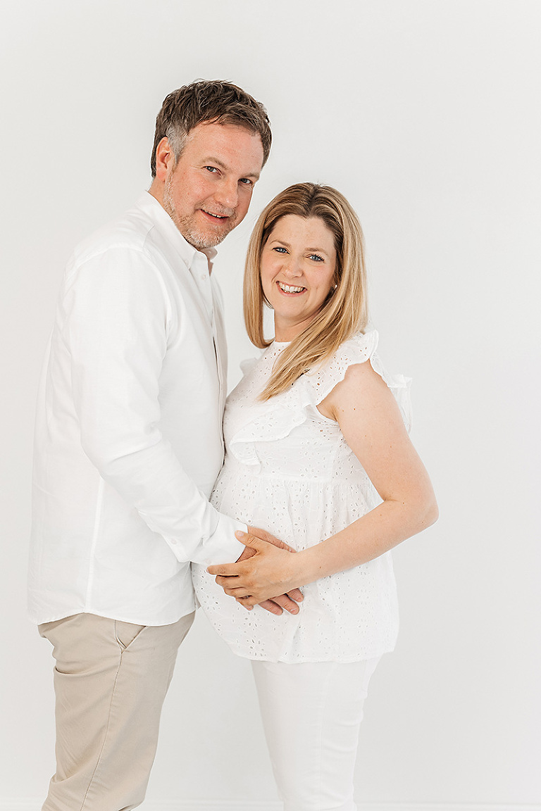 Babybauchshooting Bielefeld: Mann und schwangere Frau stehen nebeneinander und lächeln in die Kamera